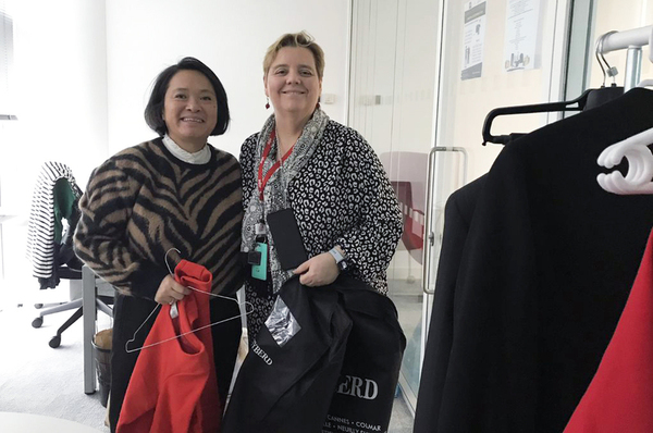 2 women hold clothes and hangers near rack in office