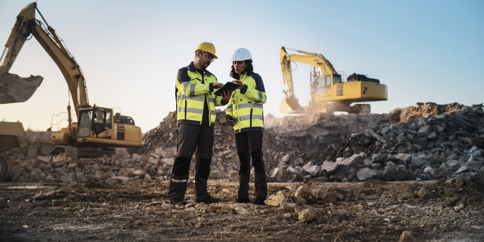 Caucasian Male Civil Engineer Talking To Hispanic Female Inspector and Using Tablet On Construction Site