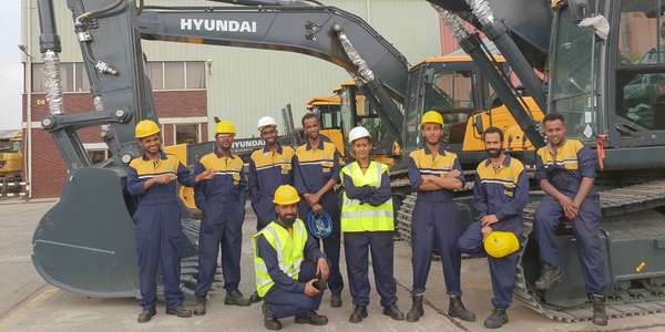 workers in uniforms and yellow hardhats stand in front of excavators