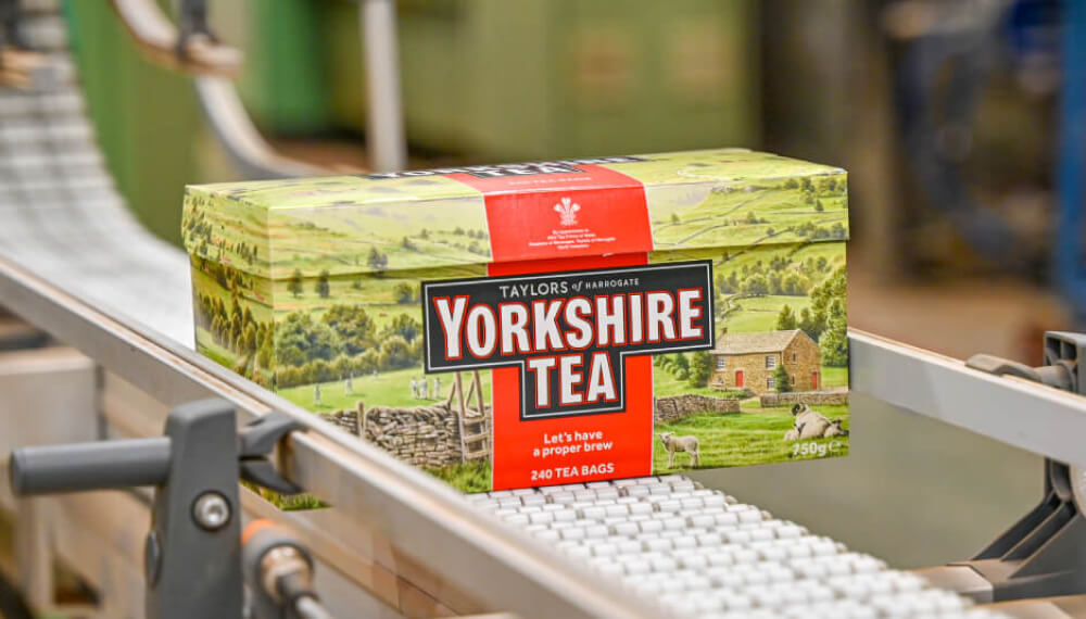Closeup of a box of Taylors of Harrogate tea on a conveyor belt inside a manufacturing factory