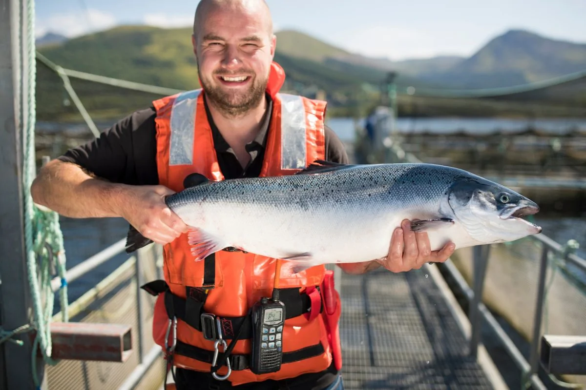 A middle-aged man, holding a salmon, smiling