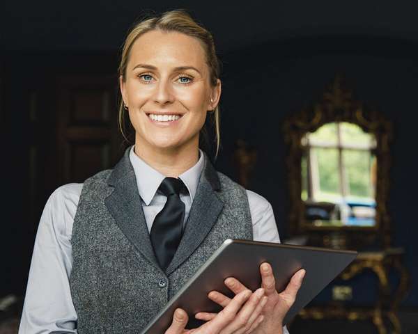 An employee is holding an iPad with a restaurant in the background