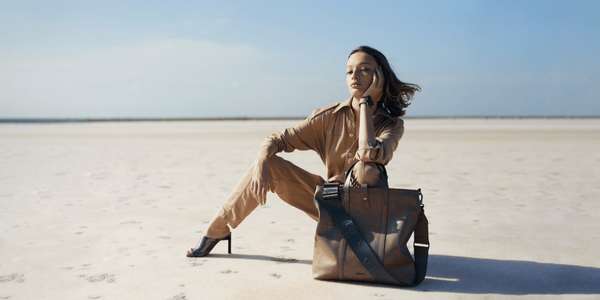 woman seated on a flat plain wearing shirt pants high heels large leather bag