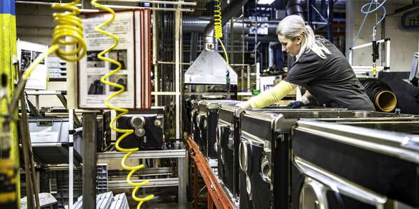 Female worker assembling home appliance on conveyer belt in factory