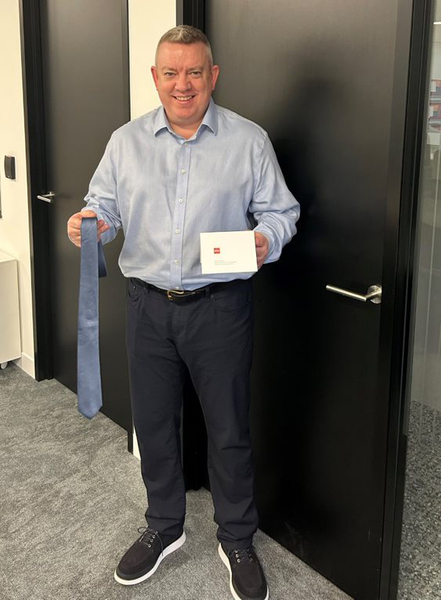 Man Ben Perry holds necktie and card standing in office hallway outside closed black doors