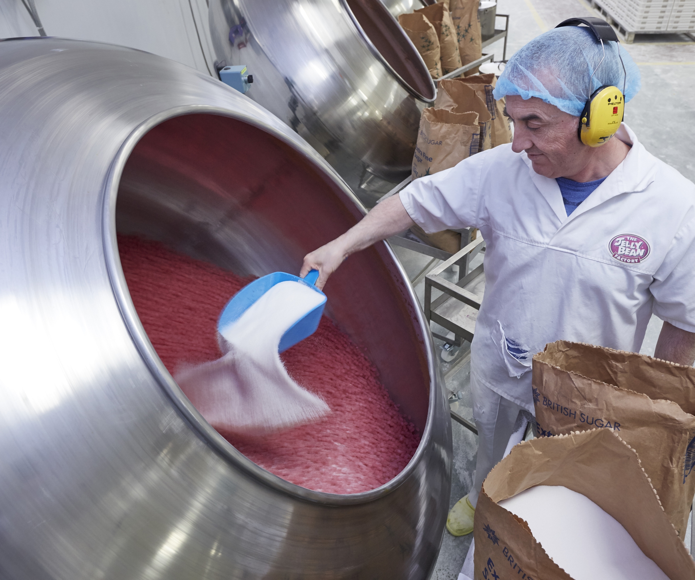 Photo of a man dressed in a white uniform scooping sugar at the food plant