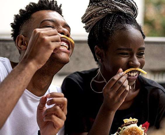 Two teenagers seated at a fast food restaurant laughing with French fry mustaches.