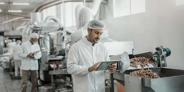 supervisor evaluating quality of food in food plant while holding tablet.