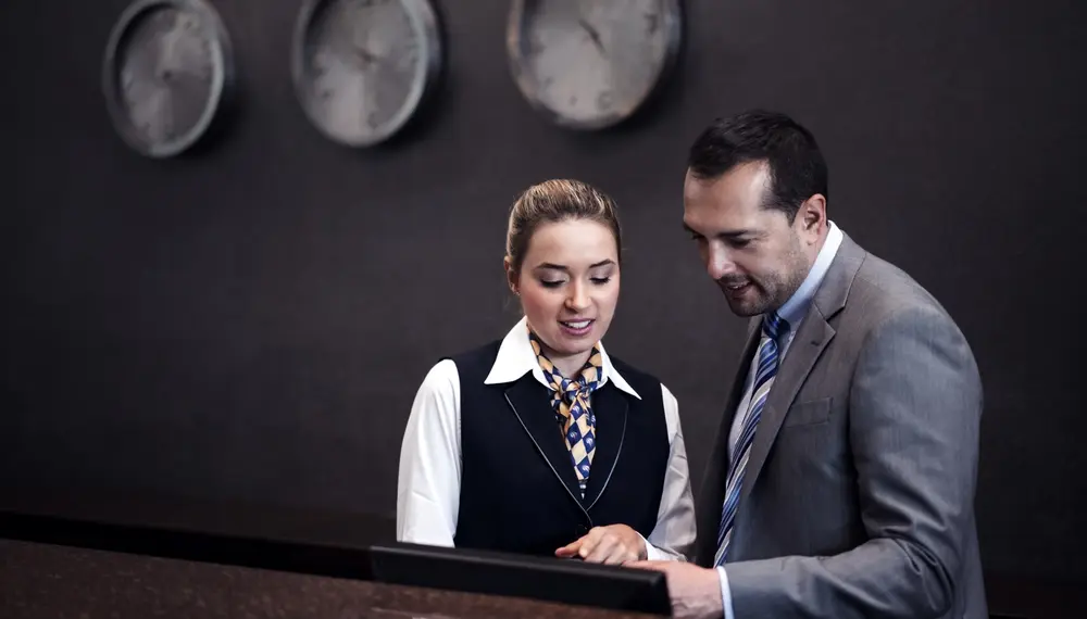 A hotel manager explains a specific room arrangement with reception staff at the front desk