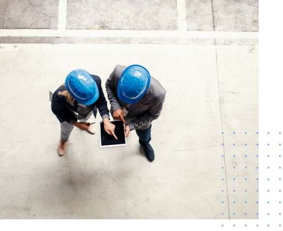 Blick von oben auf zwei Fabrikarbeiter im Werk, die sich ein Tablet mit dem Produktions- und dem Auftragsmanagement ansehen