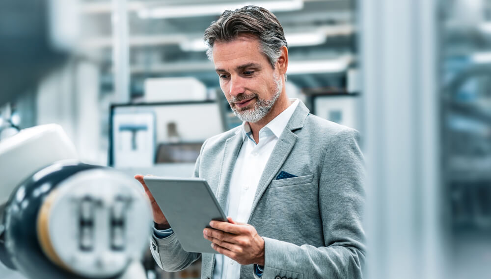 Businessman working on his tablet standing in front of a new assembly robot inside a lab