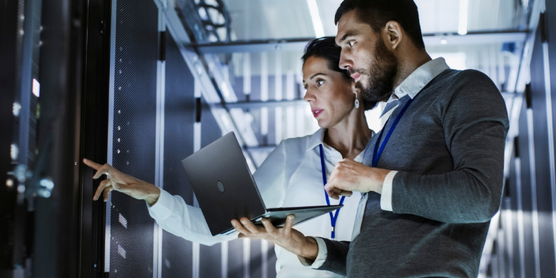 it specialist holds laptop and discusses work with female server technician