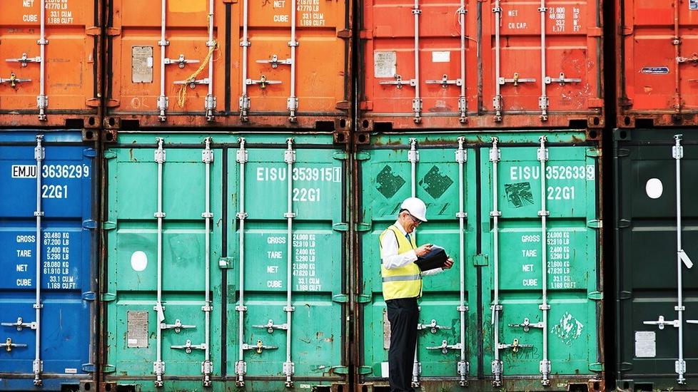 Worker using ESG software on a tablet in front of shipping containers 