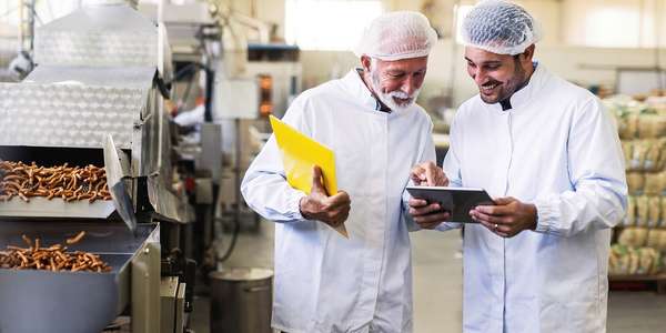 Two food manufacturing workers looking at modern cloud-based food and beverage software to help reduce waste and minimize food safety risks.