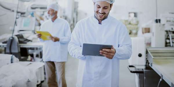 supervisor in sterile white uniform using tablet while standing in food plant