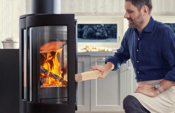 Man adding firewood to Jøtul fireplace