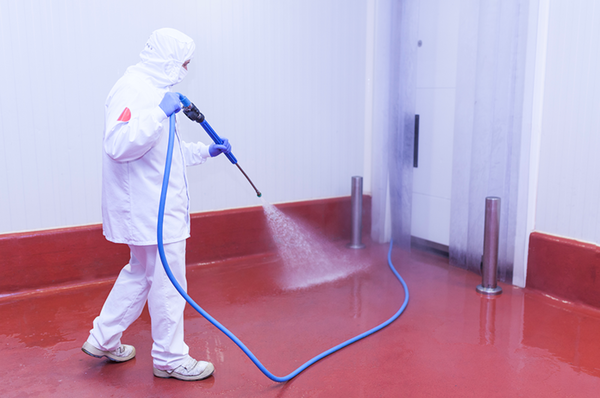 person in white protective suite spraying hose red floor white walls