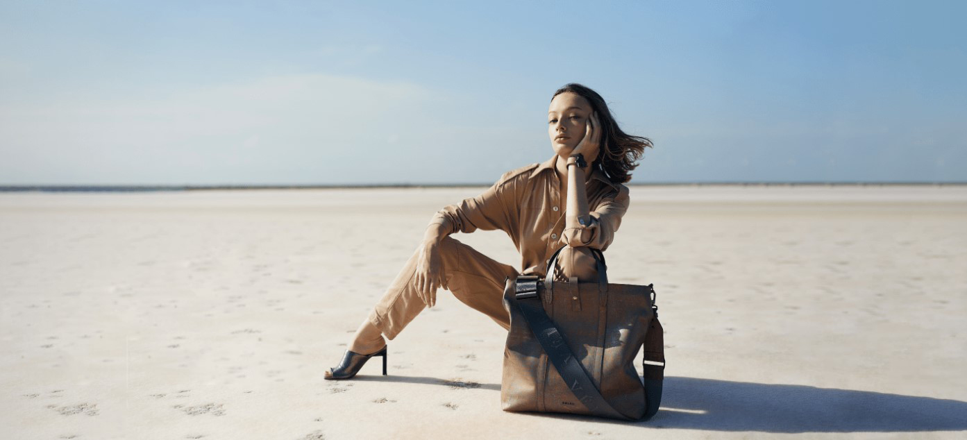 woman seated on a flat plain wearing shirt pants high heels large leather bag