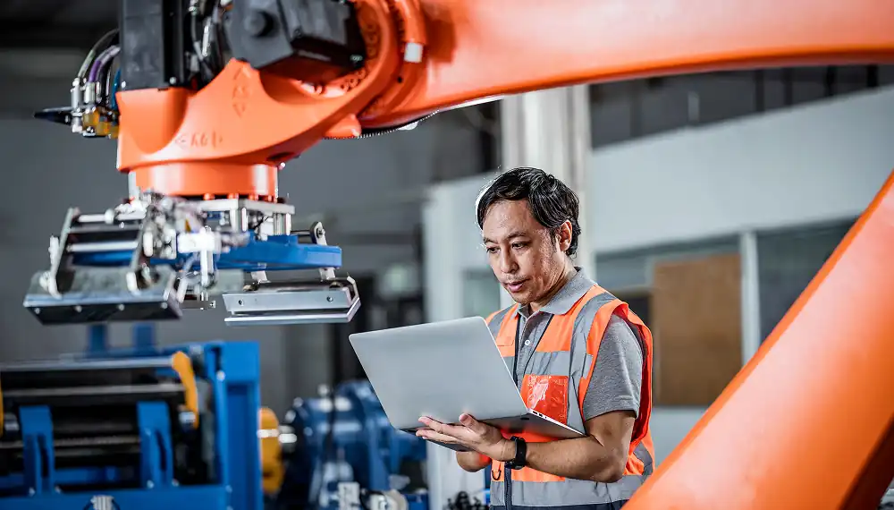 Man on laptop in front of robotic arm