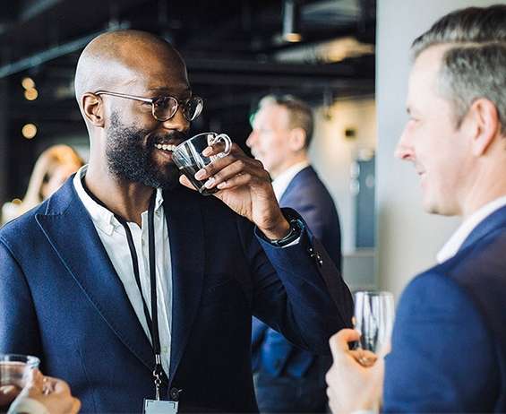 A gathering of professionals at a live event in a hotel function space greet each other and talk