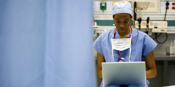 nurse scrubs stethoscope sitting laptop   hospital bed  