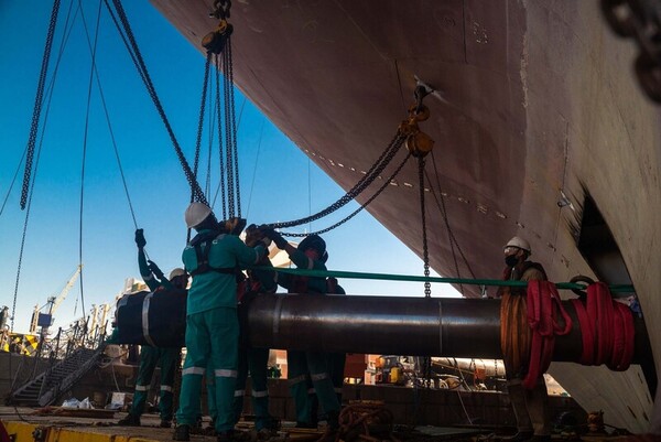 crew maneuvers metal shaft into place in ship repair in drydock