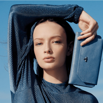 headshot of woman in blue short holding blue leather handbag by her head