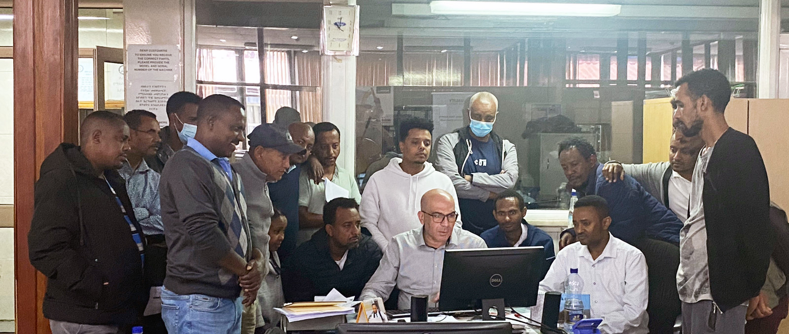 12 men gather around and stare at laptop in office