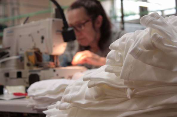 woman working at a sewing machine with white clothing in front of her