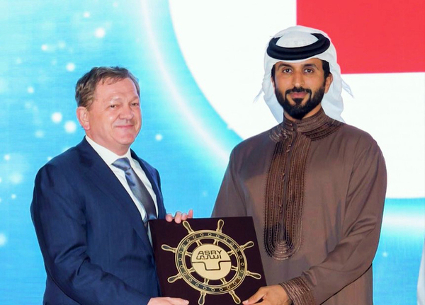 man in suit man in brown robe white head scarf hold award 