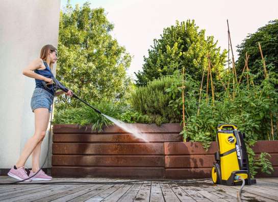 woman spraying outdoor deck with a power washer