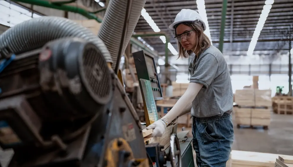 Female worker in a lumber warehouse inspecting a production machine