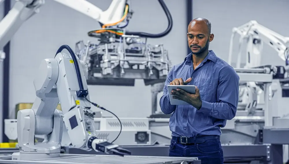 Engineer using a tablet to control robots in a factory