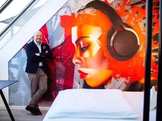 photo of the managing director of hotel am triller in front of a mural in the hotel