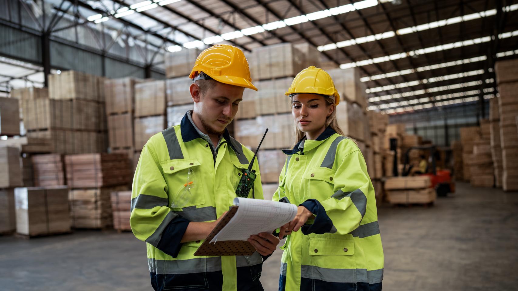 Warehouse managers on the warehouse floor in yellow vests and hard hats