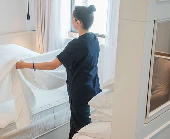 A hotel houskeeping service worker makes a bed in a guest room