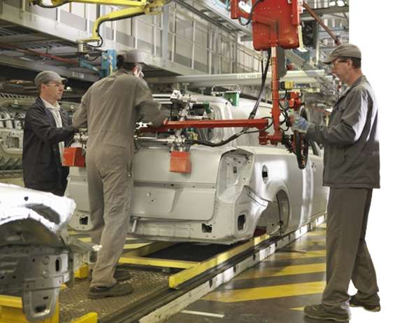 Ouvrier automobile inspectant des véhicules sur une chaîne de production.