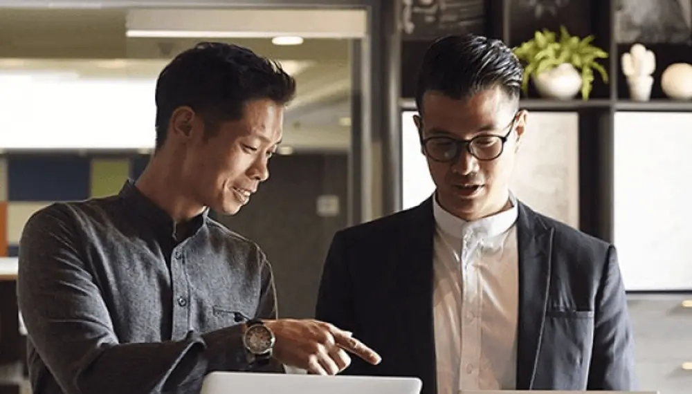 Two male colleagues are having a close discussion over expense reports on their laptops