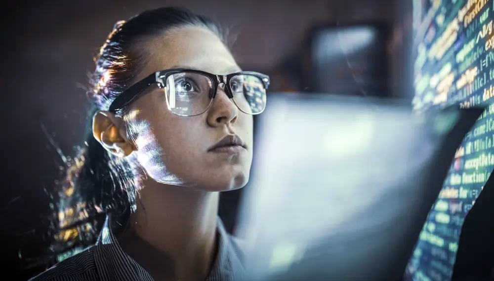 Numbers on a computer screen reflected in a woman’s glasses