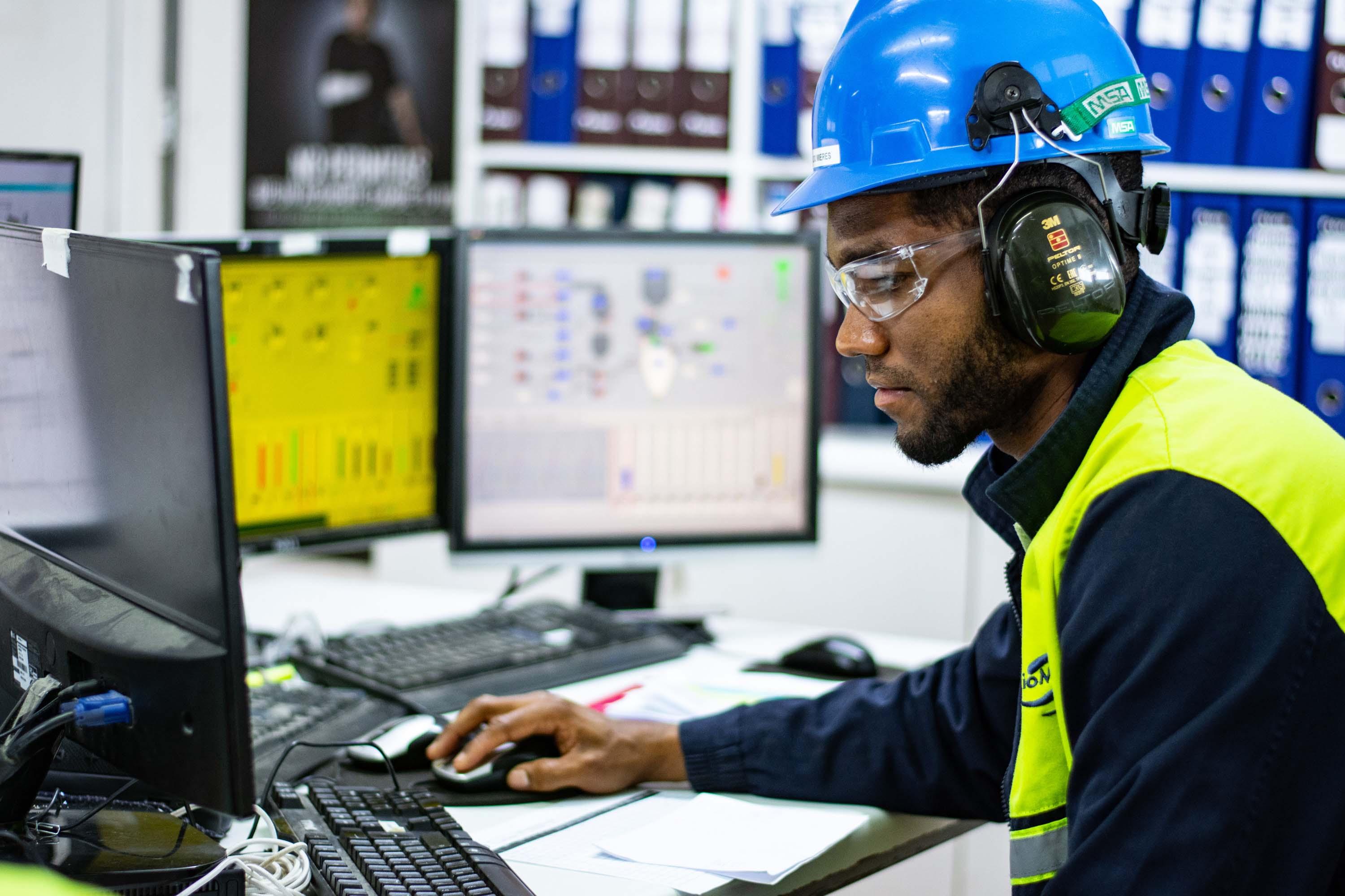 man working on computers wearing factory uniform and safety gear