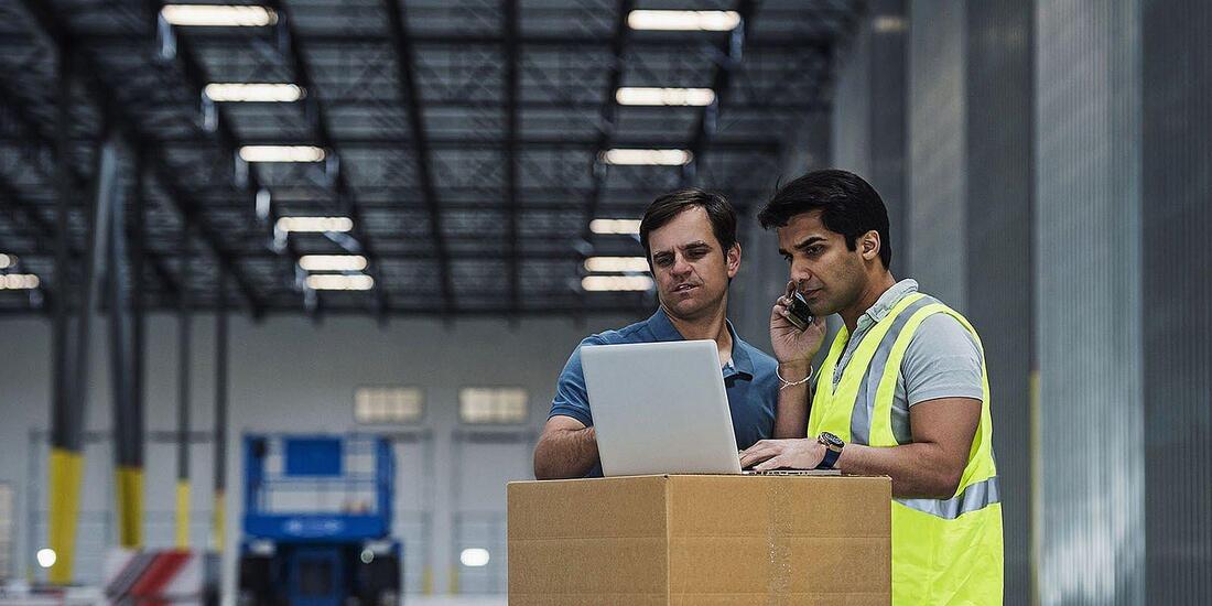 Workers using laptop and cell phone warehouse