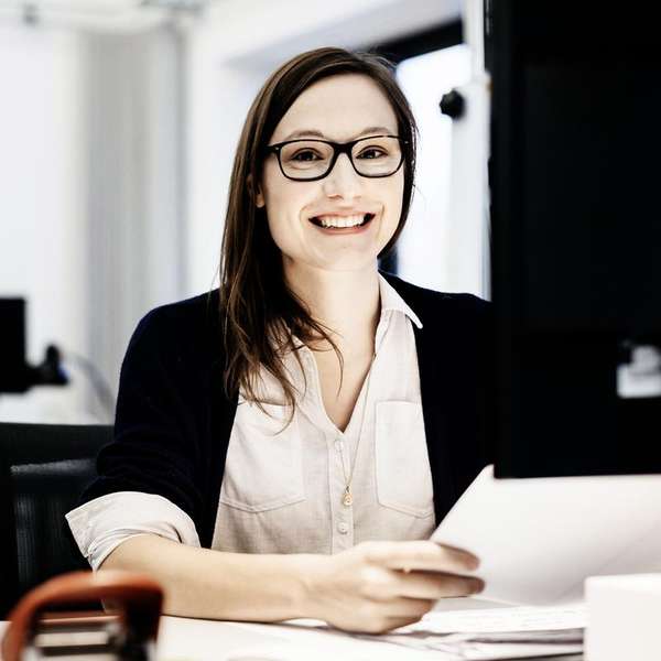 businesswoman wearing glasses is sitting in front of a computer in an office room