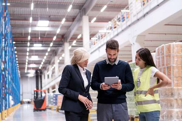 Three people using SCM software on a tablet in a warehouse