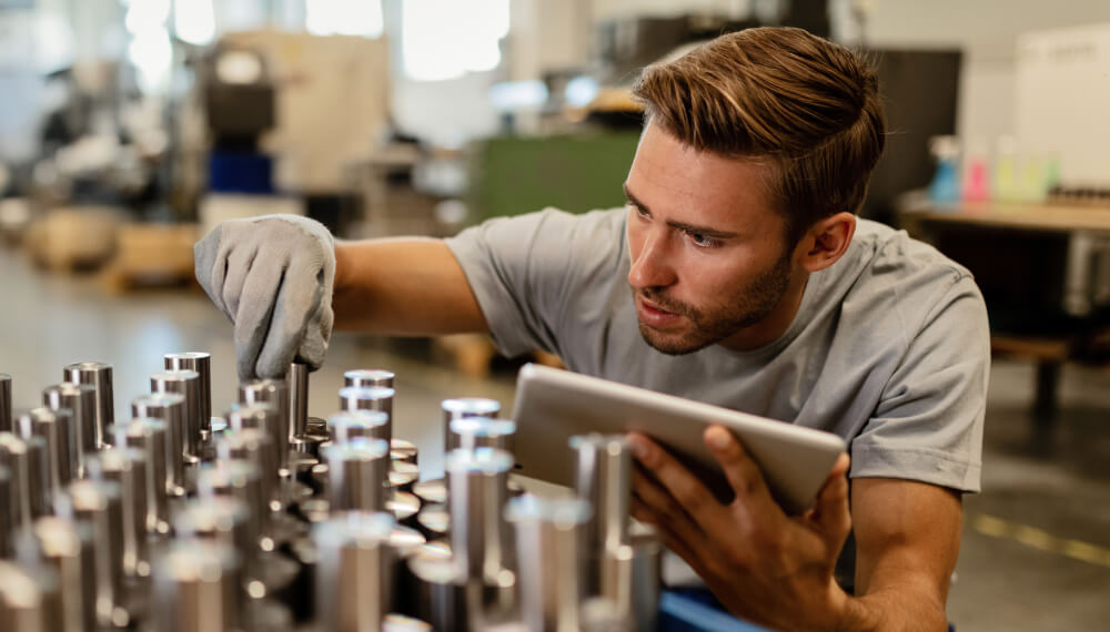 Man holding a tablet while inspecting steel manufactured products