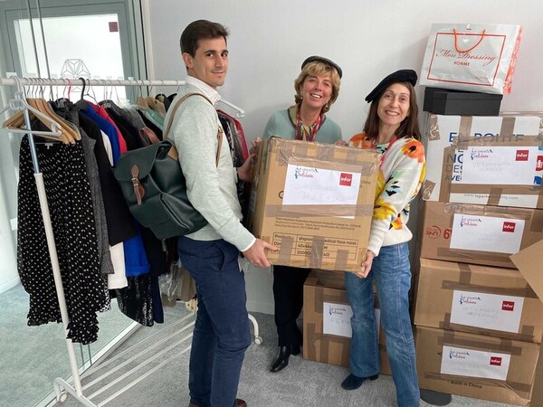 1 man and 2 women hold brown box near clothes rack and stock of boxes