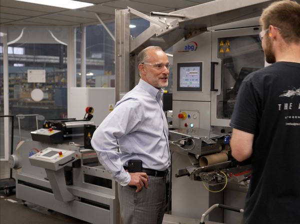 2 men stand by machine tool in factory