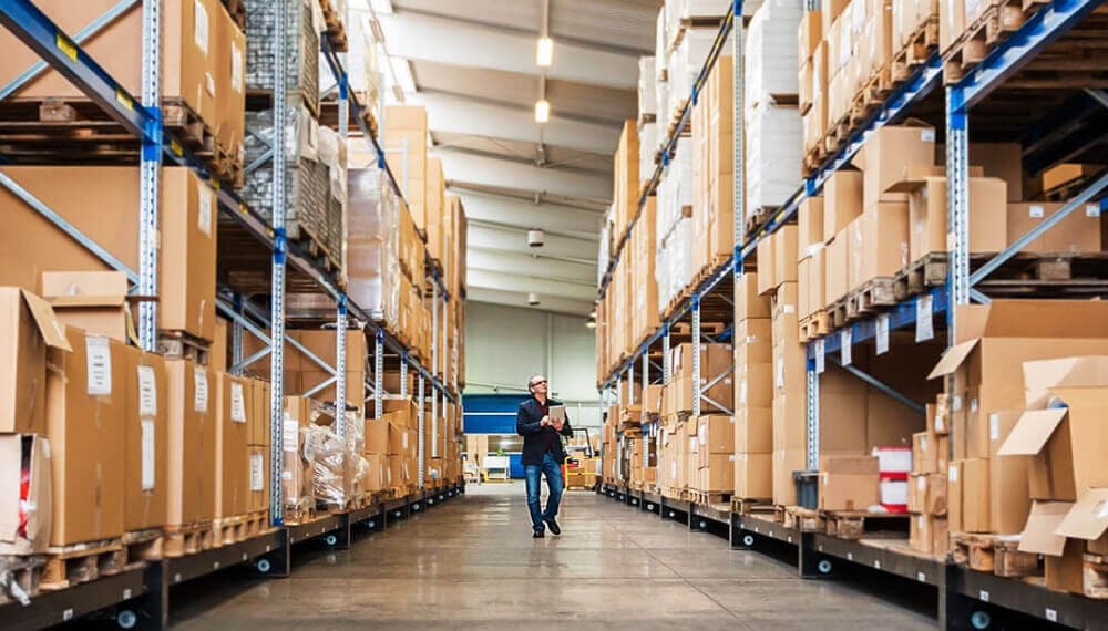 Businessman using a tablet walking down an aisle in a supply chain warehouse