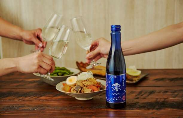 people cheering with sake glasses next to plates of japanese food