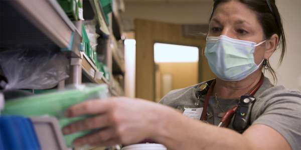 masked woman stocking hospital supply room