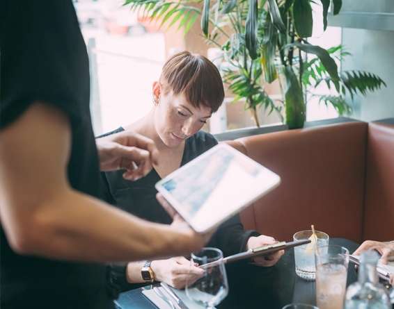 A restaurant server taking an order with a tablet POS at a table with two patrons holding menus in their hands